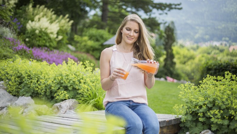 Relaxing in the alpine garden., © Patrick Haberler Woman sits in the garden and pours juice into a glass.