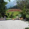 Wanderstartplatz, © Forellenhof Eingang zu einem Wanderstartplatz mit Bänken und einem Schild, umgeben von Bäumen und Bergen im Hintergrund.