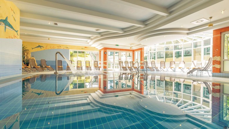 Indoor swimming pool, © Hotel Schneeberghof A bright indoor pool with sun loungers and a jet of water in the pool.