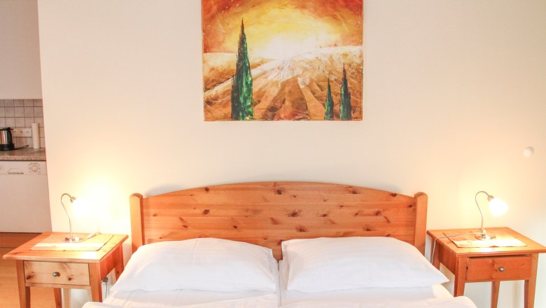 Wohnung 30m², © Haus Lenz Schlafzimmer mit Holzbett, zwei Nachttischen und einem Landschaftsbild an der Wand.