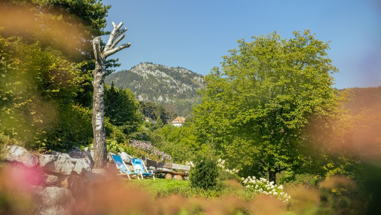 Erholung im Alpengarten, © Wiener Alpen/Martin Fülöp Ein Alpengarten mit Liegestühlen, Bäumen und einem Berg im Hintergrund.
