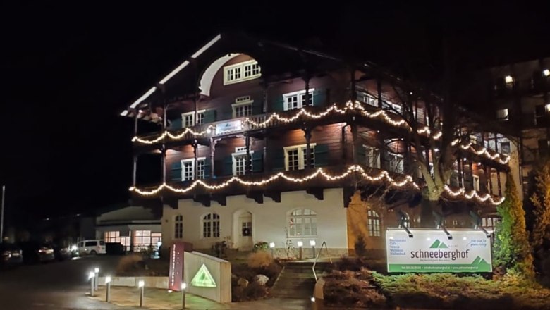 Schneeberghof in winter, © Hotel Schneeberghof An illuminated building called Schneeberghof at night, decorated with fairy lights.