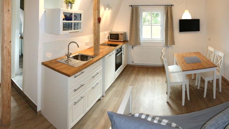 Apartment 1, © Marianne Gschaider Modern kitchen with wooden worktop, dining table and chairs in a bright room.