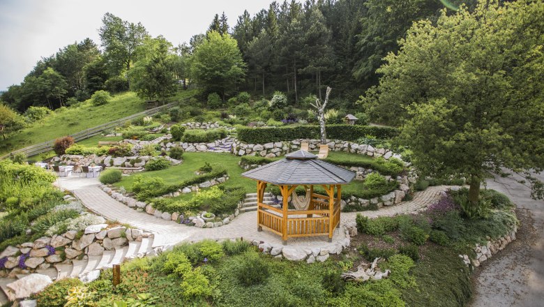 Trauungspavillion, © Patrick Haberler Ein hölzerner Pavillon in einem gepflegten Garten mit grünen Bäumen und Steinwegen.
