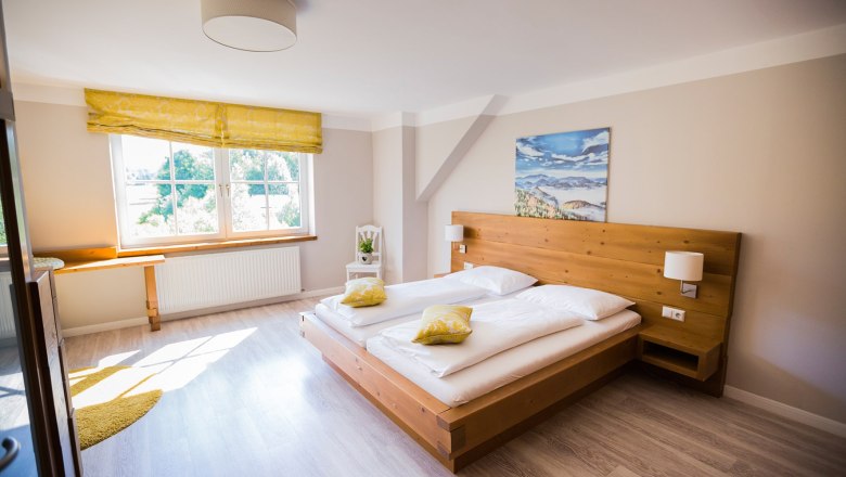 Doppelzimmer, © Patrick Haberler Helles Doppelzimmer mit Holzbett, gelben Kissen und großem Fenster.