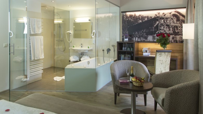 Deluxe park room, © Hotel Schneeberghof, Robert John Luxurious hotel room with glass bath, cozy armchairs, table with champagne and fruit, and a large bed with rose petals.