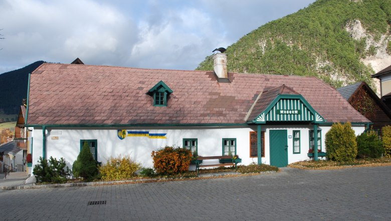 Schneebergmuseum Puchberg, © Schneebergmuseum Schneebergmuseum Puchberg, ein traditionelles Gebäude mit grünem Dach und Schornstein, umgeben von Bergen und Bäumen.