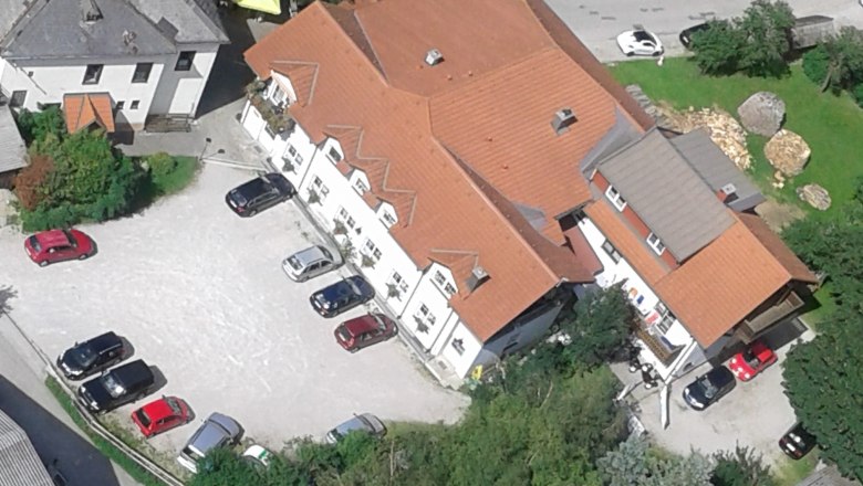 Luftaufnahme Gasthof Zwinz zum Schneeberg, © Martin Zwinz Luftaufnahme eines Gebäudekomplexes mit roten Dächern und mehreren geparkten Autos auf einem Parkplatz.
