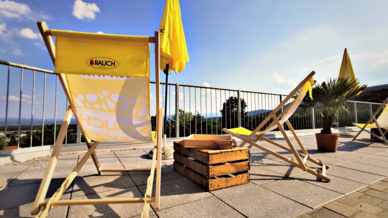 Sonnenliegen und Sonnenschirme auf einer Terrasse mit Ausblick.