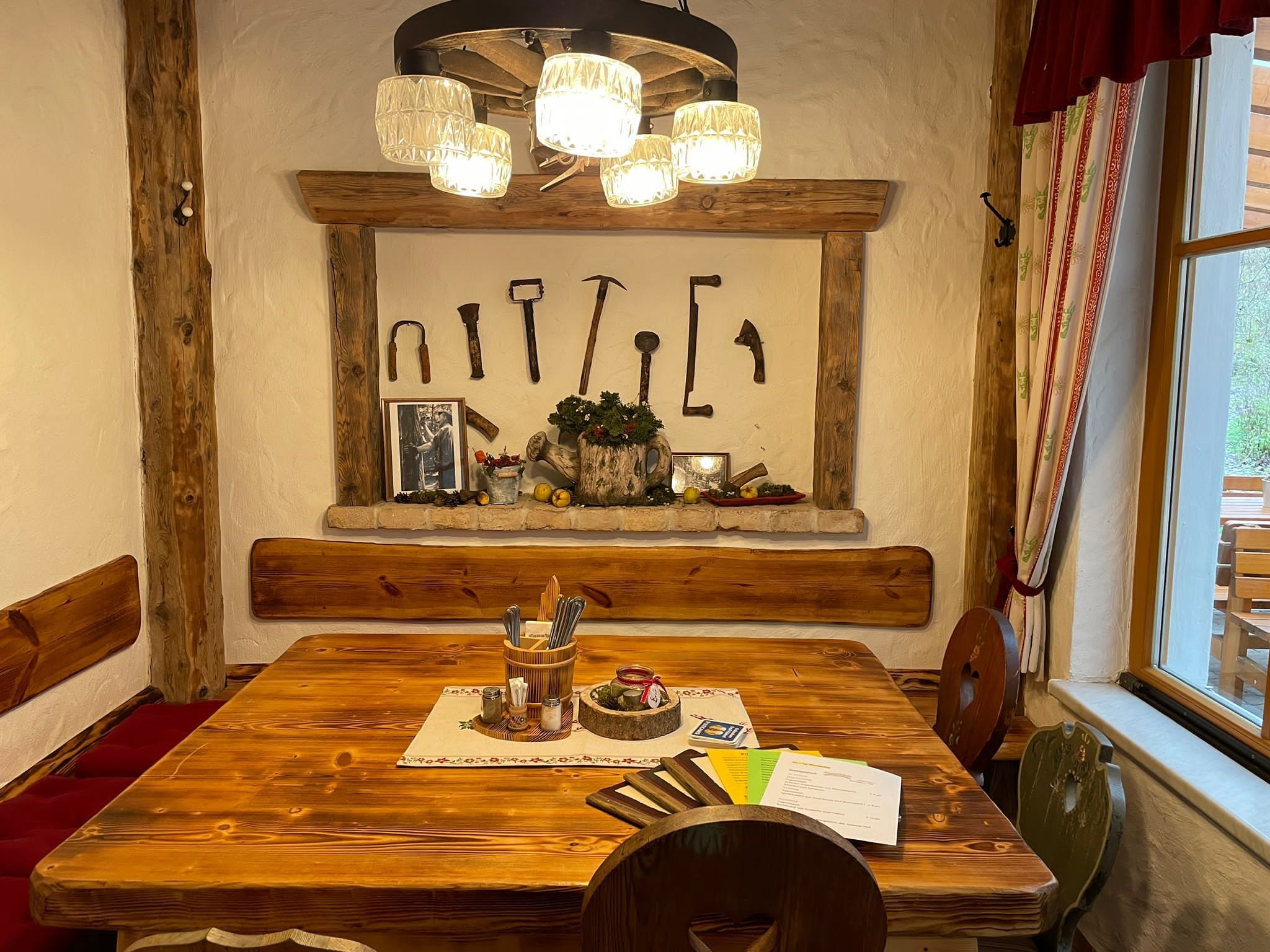 Rustikales Gastzimmer mit Holztisch, Wanddekoration aus alten Werkzeugen und gemütlicher Beleuchtung.
