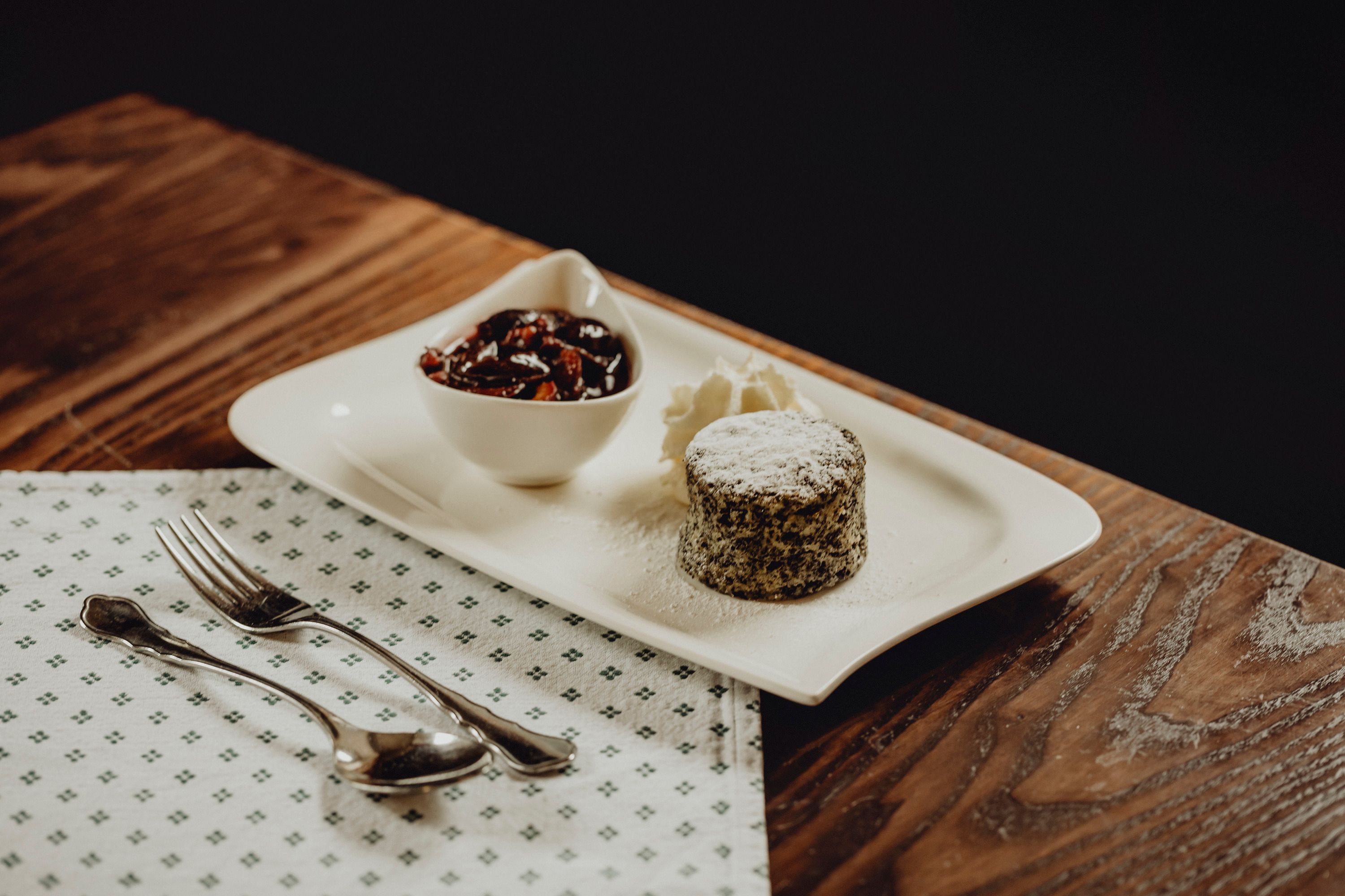 Ein Mohnkuchen mit Puderzucker, Sahne und einer Schale mit Früchten auf einem weißen Teller.