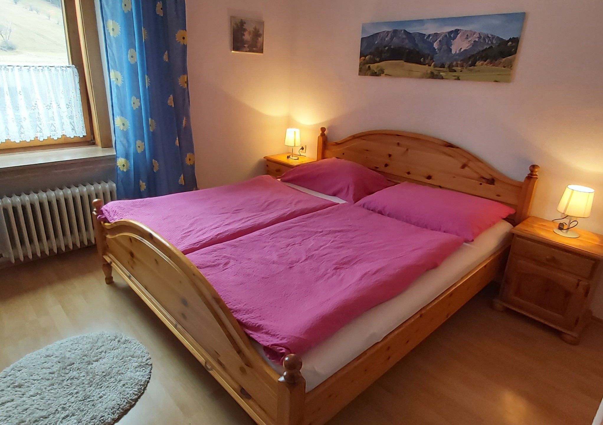 Gemütliches Doppelzimmer mit Holzbett, pinker Bettwäsche und Nachttischen mit Lampen.