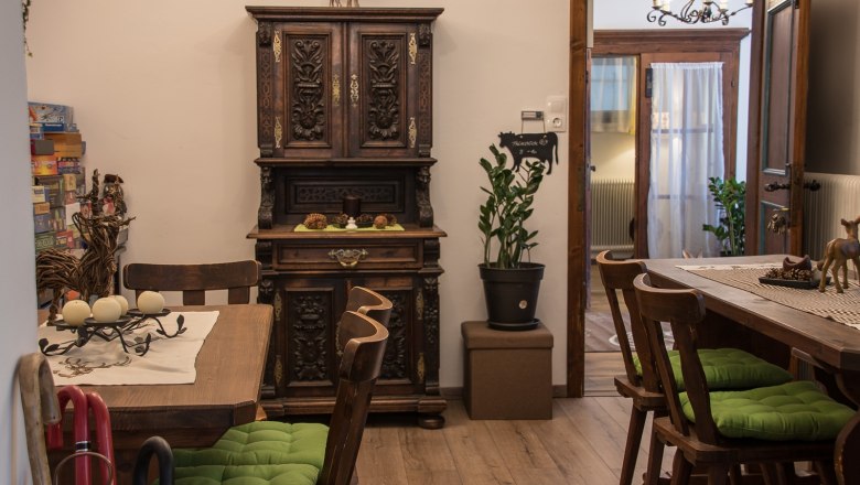 Gem&uuml;tlicher Aufenthaltsraum mit Holzm&ouml;beln, gr&uuml;nen Sitzkissen und dekorativem Schrank.