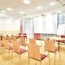 A bright seminar room with chairs, tables, a flipchart and a projection screen.