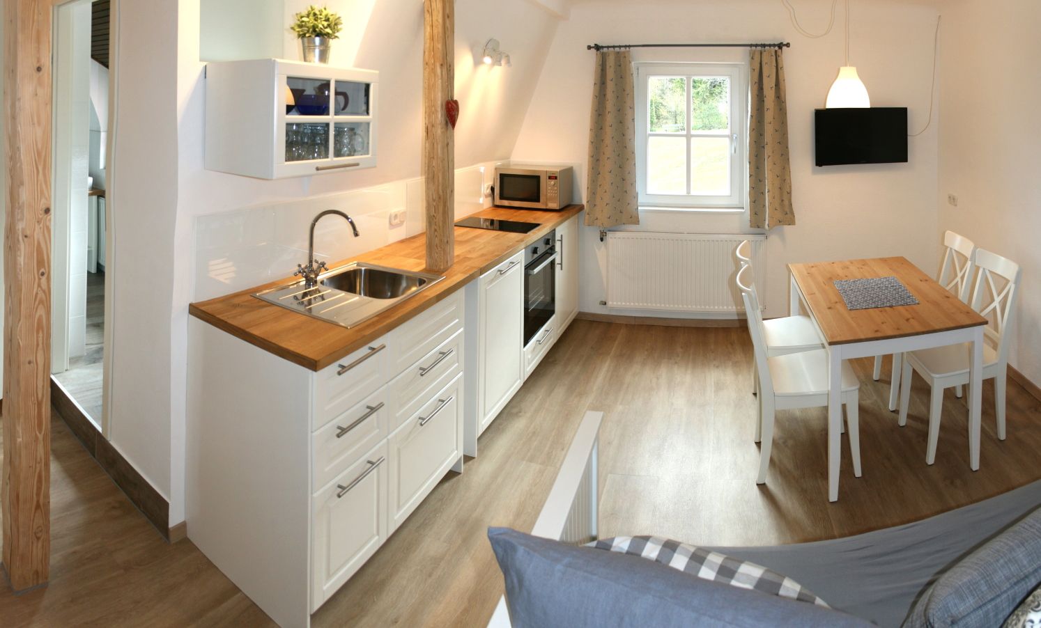 Moderne Küche mit Holzboden, weißen Schränken, Esstisch und Fenster.