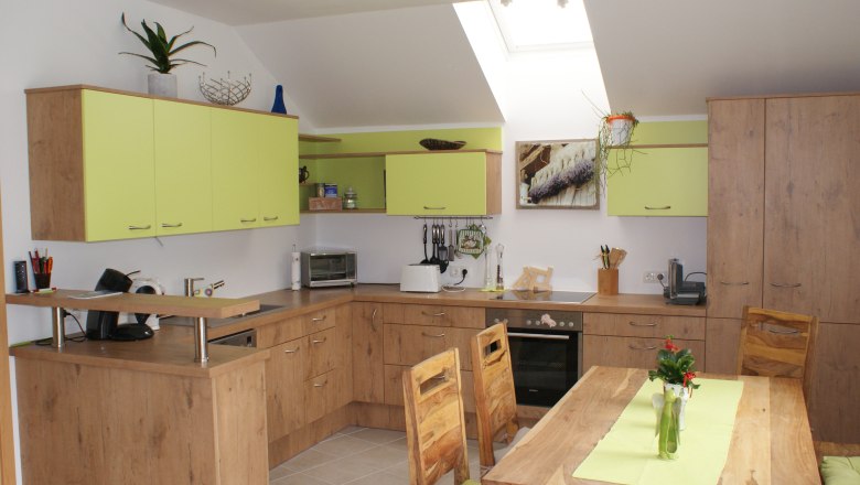Modern kitchen with wooden furniture and green accents, dining table with vase, skylights.