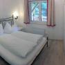 Schlafzimmer in einem Ferienhaus mit Doppelbett, TV und Fenster mit Vorh&auml;ngen.