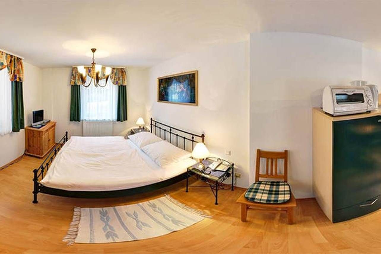 Kleines Schlafzimmer mit Doppelbett, Nachttischen, TV, Mikrowelle und Stuhl.