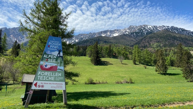 Sign in front of a mountain landscape with meadow and trees.