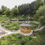 Ein h&ouml;lzerner Pavillon in einem gepflegten Garten mit gr&uuml;nen B&auml;umen und Steinwegen.