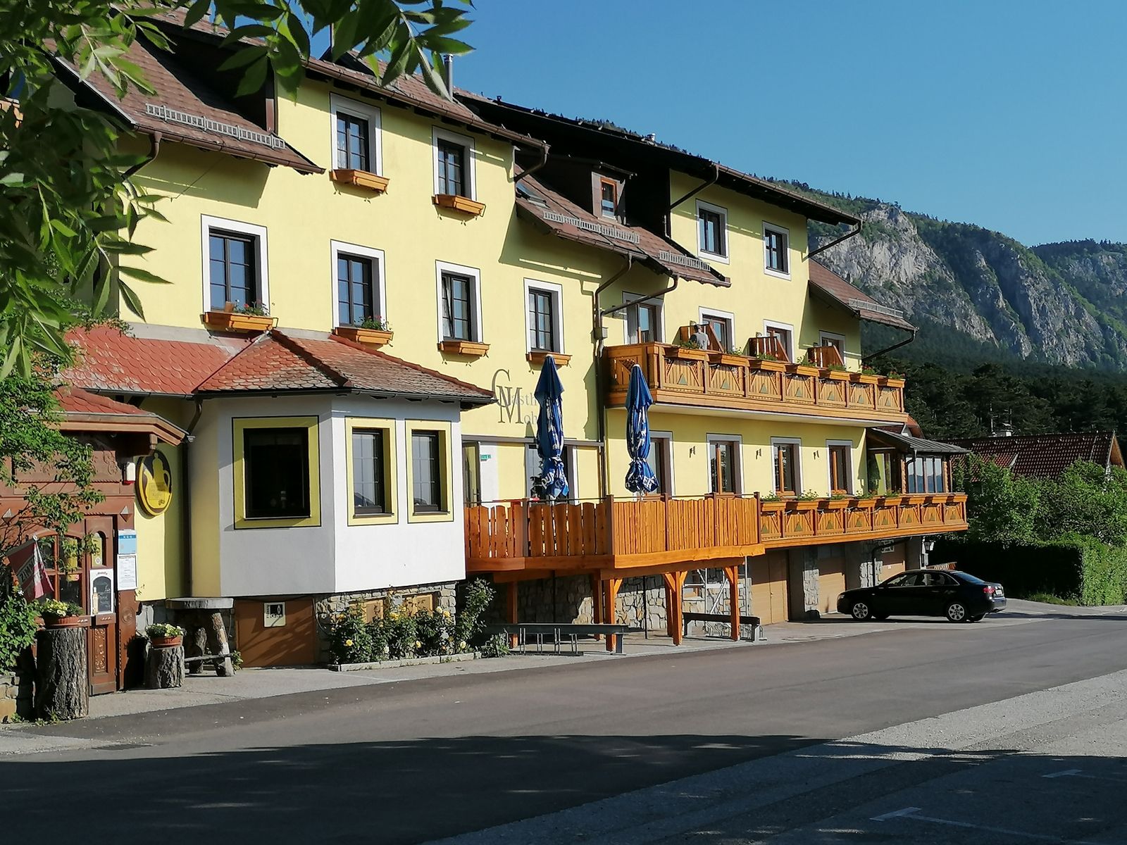 Gelbes Gasthaus mit Holzbalkonen und Berg im Hintergrund.
