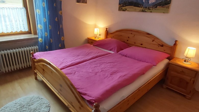 Cozy double room with wooden bed, pink bed linen and bedside tables with lamps.