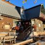 A rustic wooden house with flowers and benches outside in the sunshine.