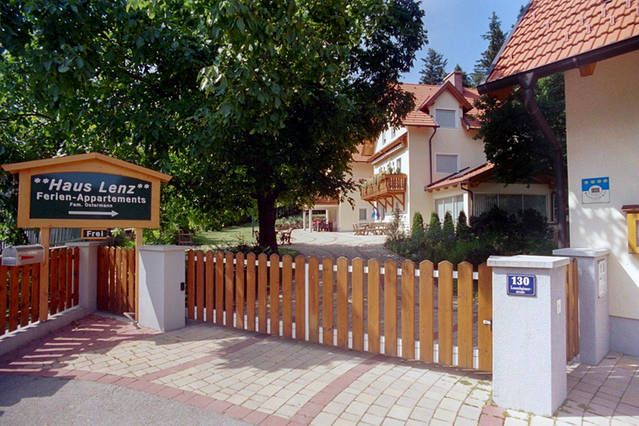 Eingang zu Haus Lenz mit Holzzaun und Schild, umgeben von Bäumen.