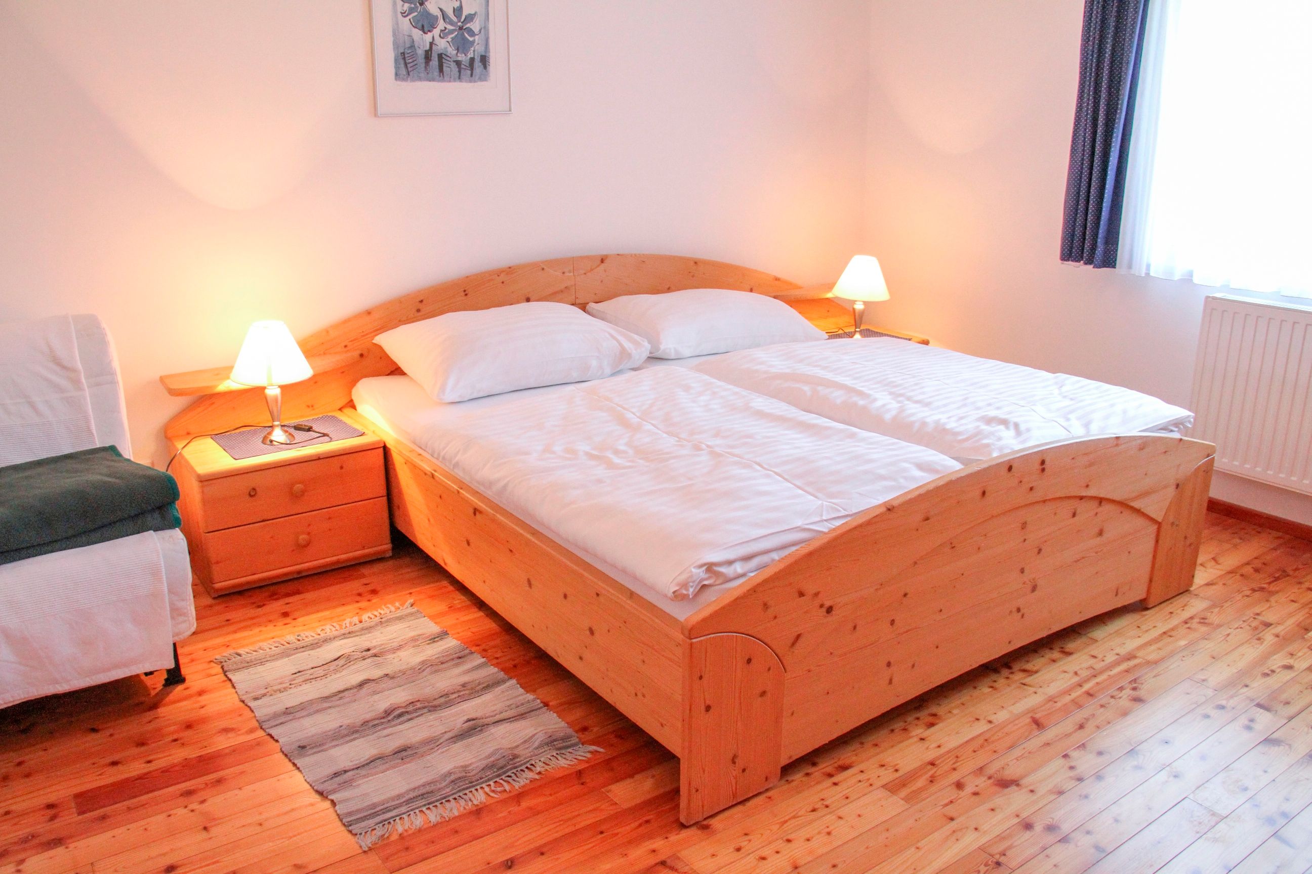 Gemütliches Schlafzimmer mit Doppelbett, Holzboden und Nachttischen mit Lampen.