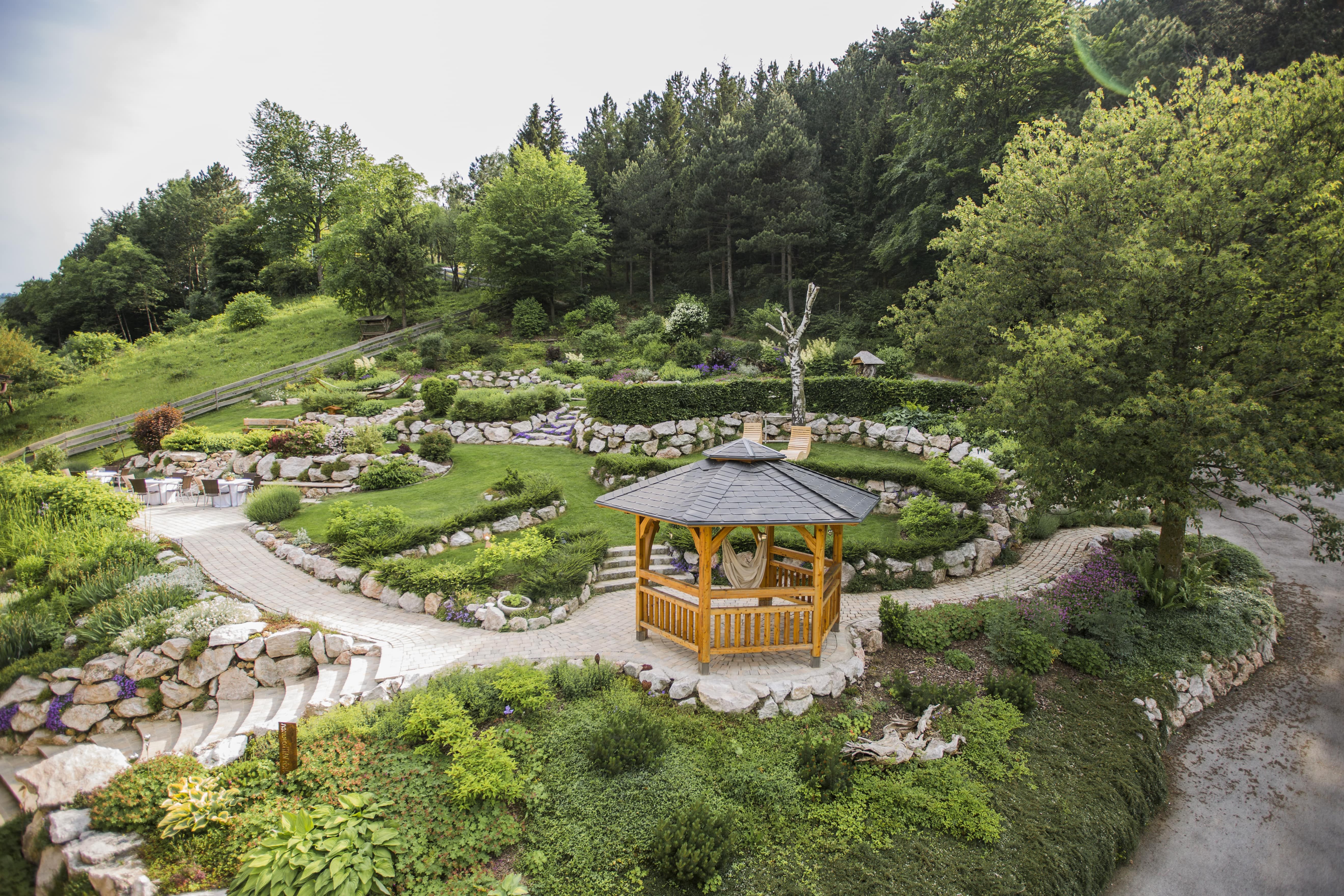 Ein hölzerner Pavillon in einem gepflegten Garten mit grünen Bäumen und Steinwegen.