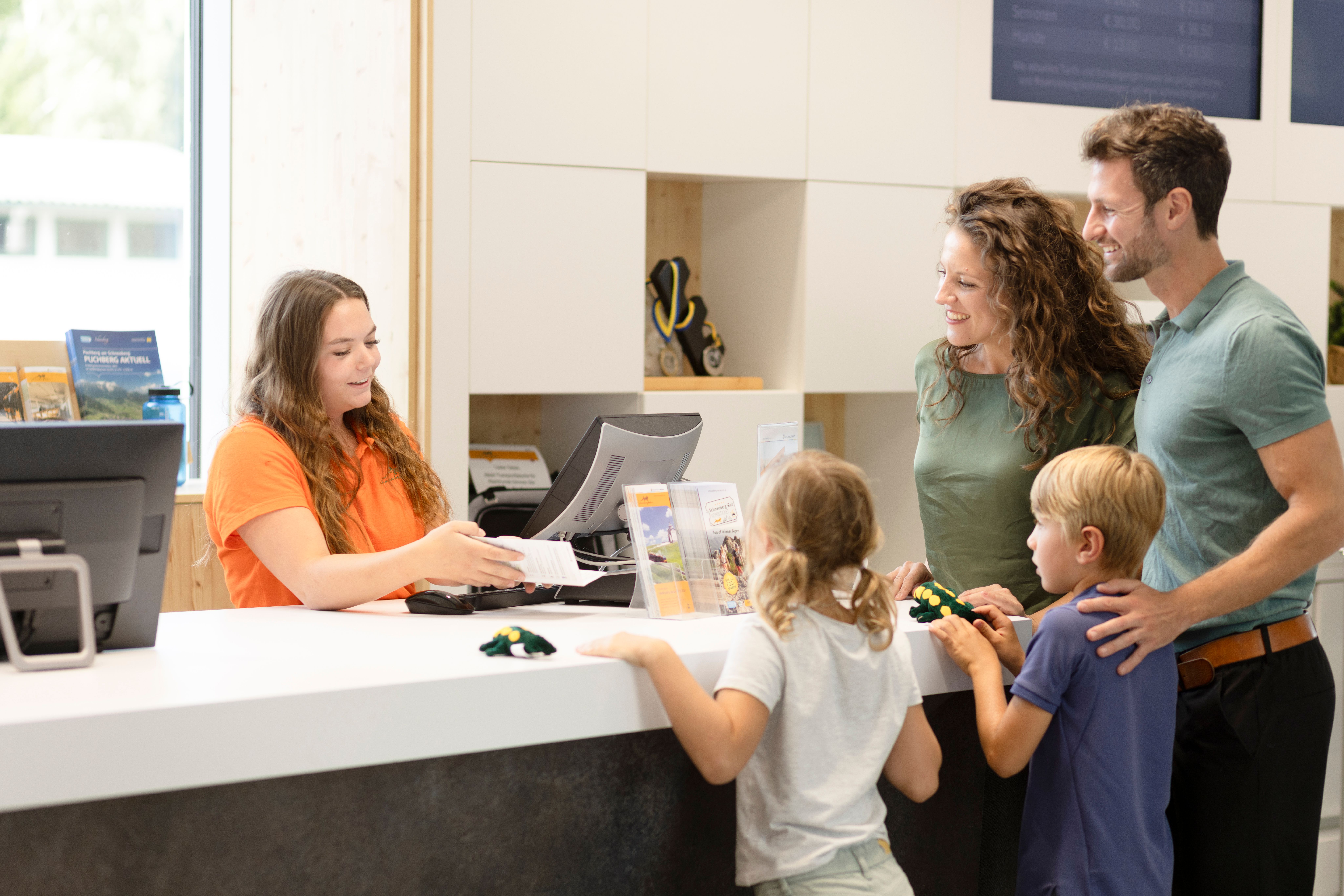 Familie mit zwei Kindern wird an einer Rezeption von einer Mitarbeiterin beraten.