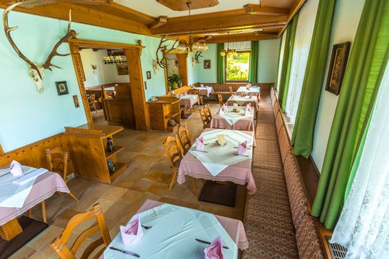 Gemütliches Restaurant mit Holzmöbeln und Tischdecken, dekoriert mit Geweihen an den Wänden.
