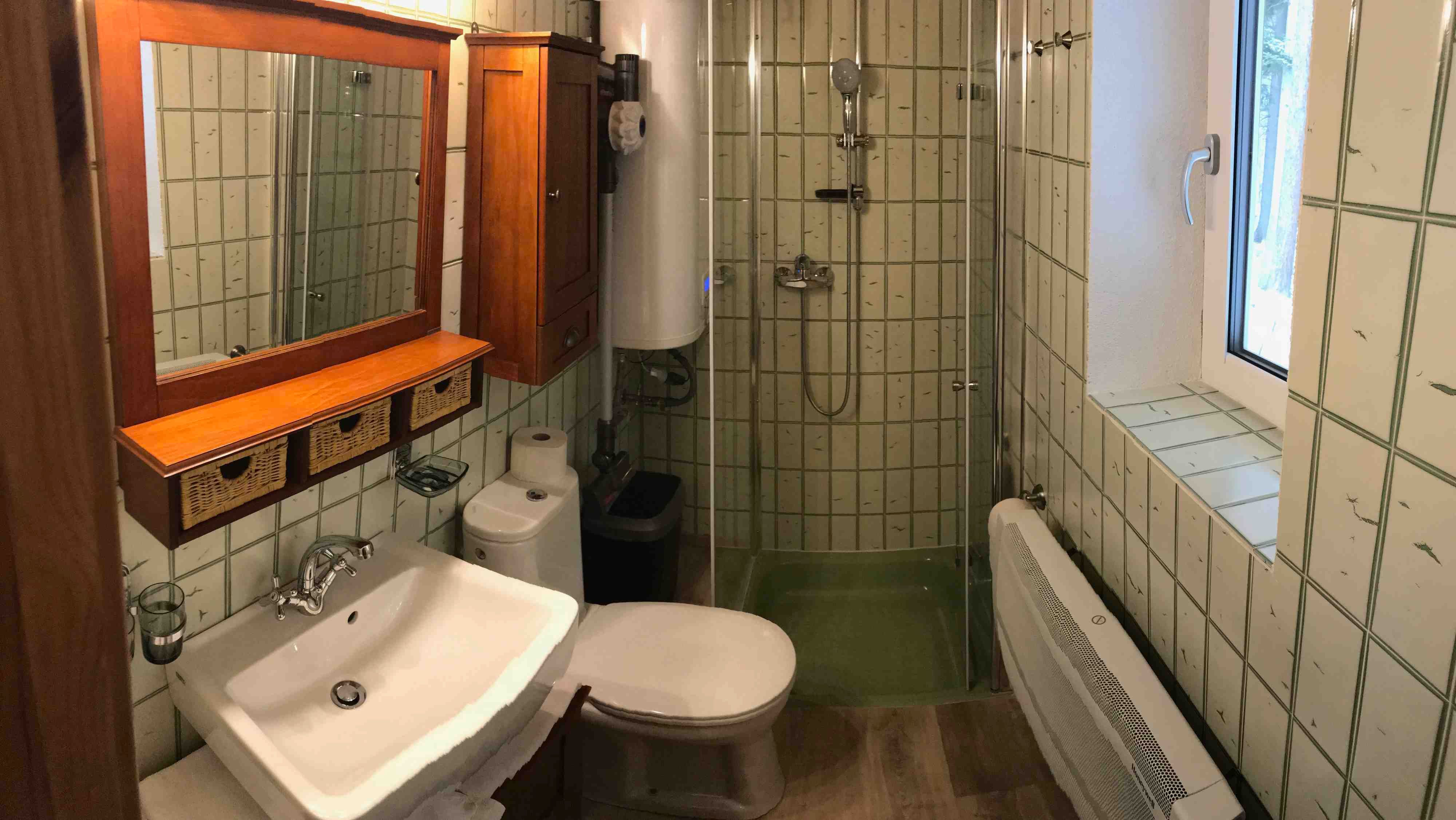 Kleines Badezimmer mit Dusche, Waschbecken, Toilette und Holzschränken.