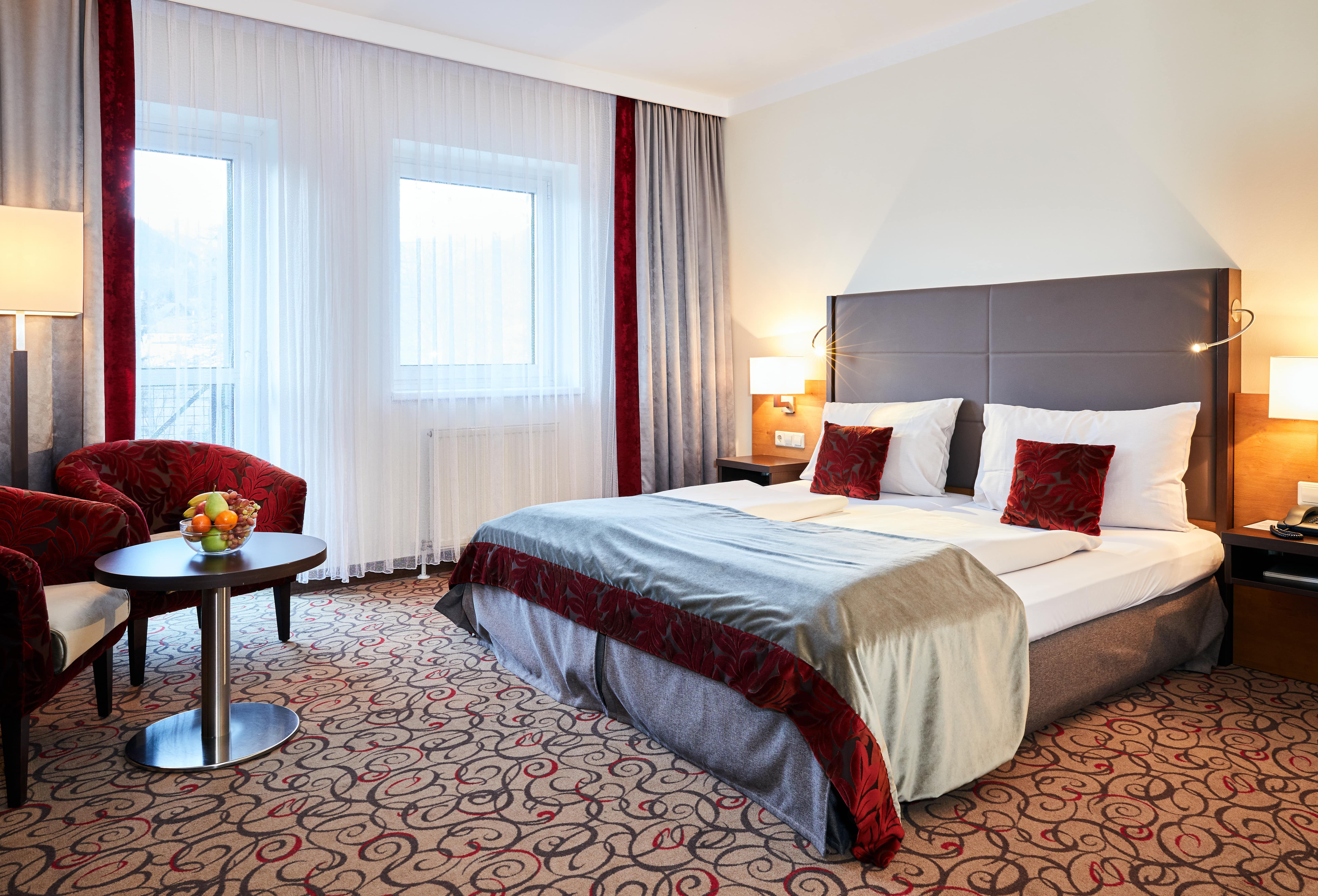 Doppelzimmer im Hotel Schneeberghof mit Doppelbett, roten Kissen, Tisch mit Obstschale und zwei Sesseln.