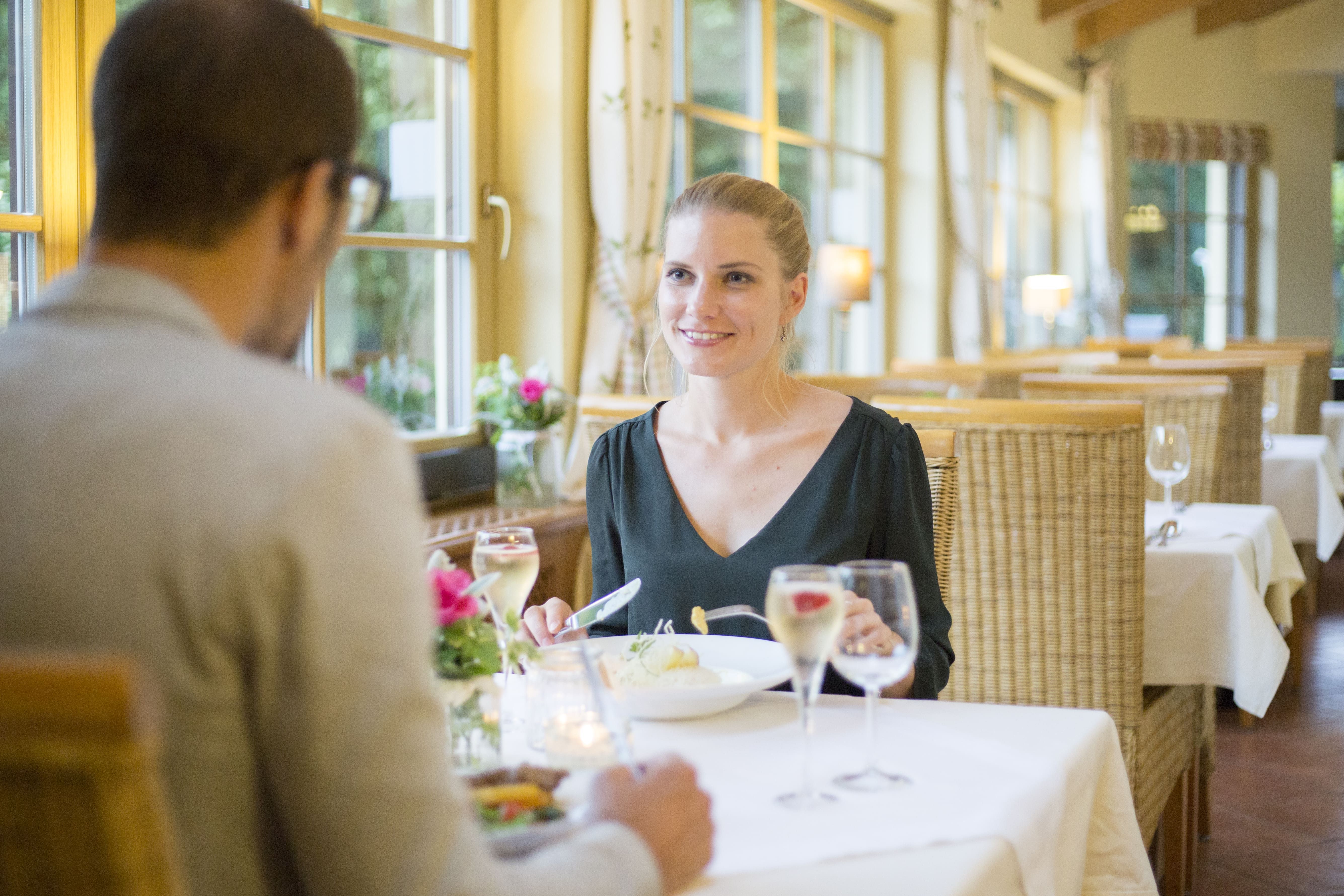 Ein Paar beim Abendessen in einem gemütlichen Restaurant mit großen Fenstern und Kerzenlicht.