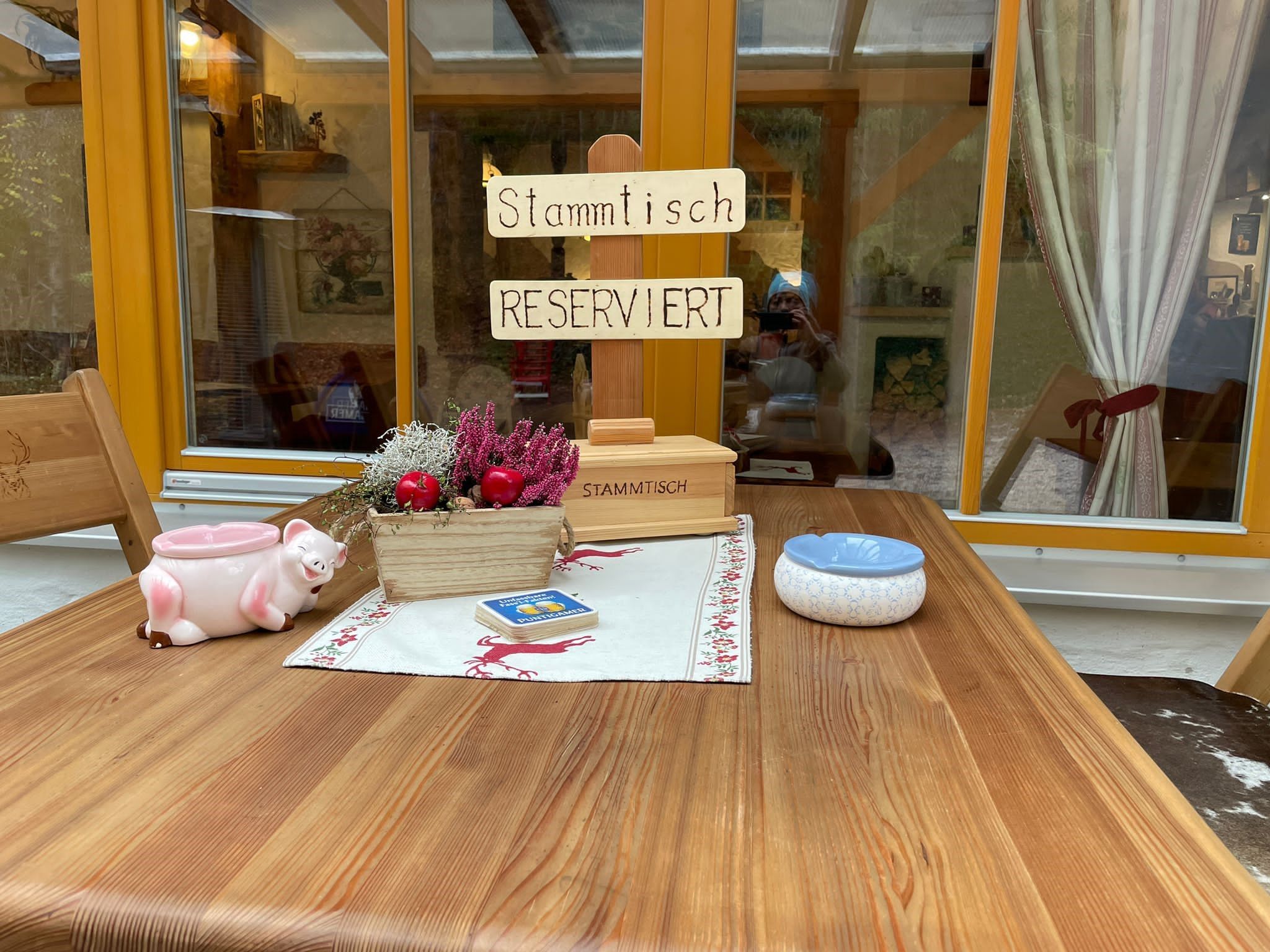 Ein rustikaler Tisch mit einem Schild 'Stammtisch Reserviert', Dekorationen und einem Aschenbecher.