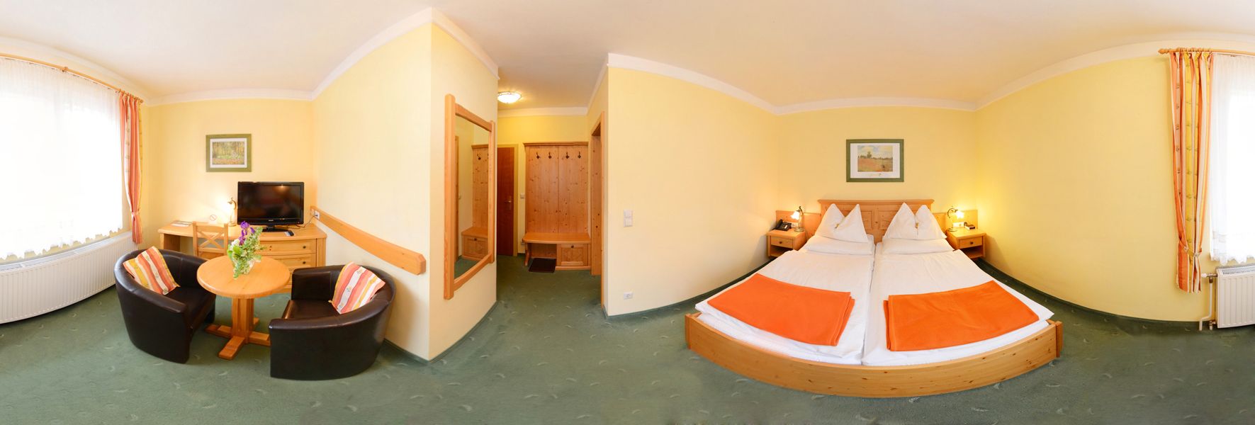 Panorama eines Hotelzimmers mit Doppelbett, Tisch, zwei Sesseln und Fernseher.