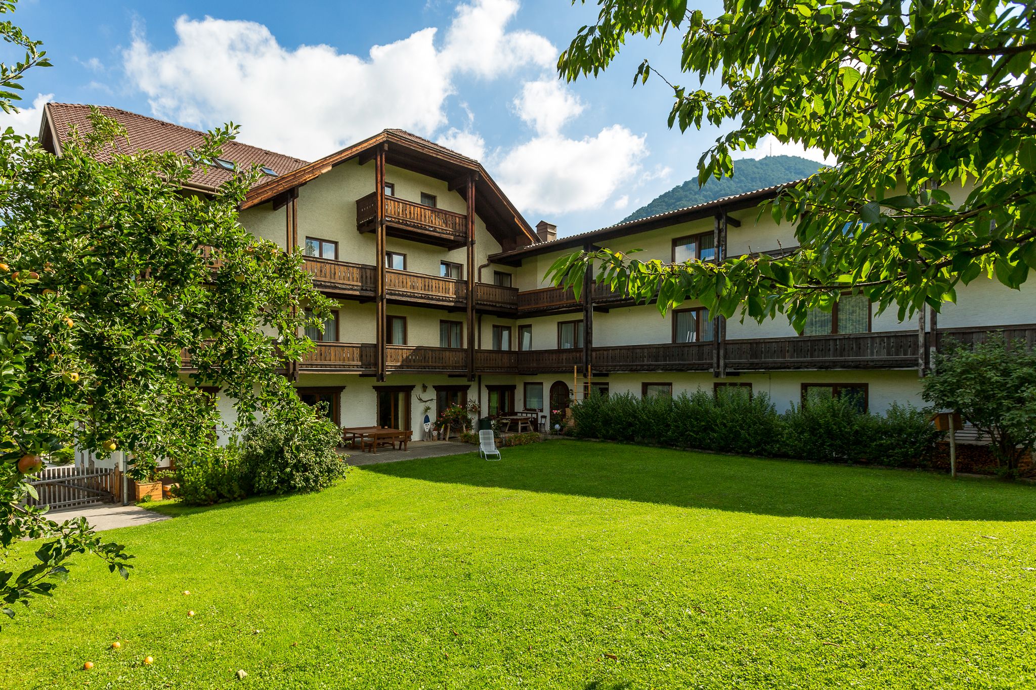 Ein traditionelles Hotel mit Holzbalkonen und einem gepflegten Garten im Vordergrund, umgeben von Bäumen und Bergen im Hintergrund.