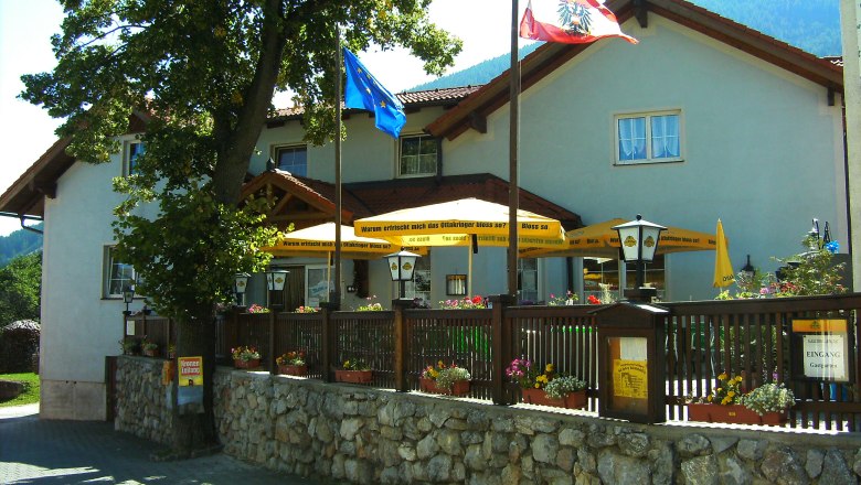 Gasthof Zwinz with terrace and parasols, surrounded by flowers and flags.