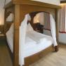 Gem&uuml;tliches Schlafzimmer mit Himmelbett, angrenzendem Badezimmer und Balkonzugang.