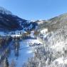 Winter landscape with snow-covered mountains and a farm in the valley.