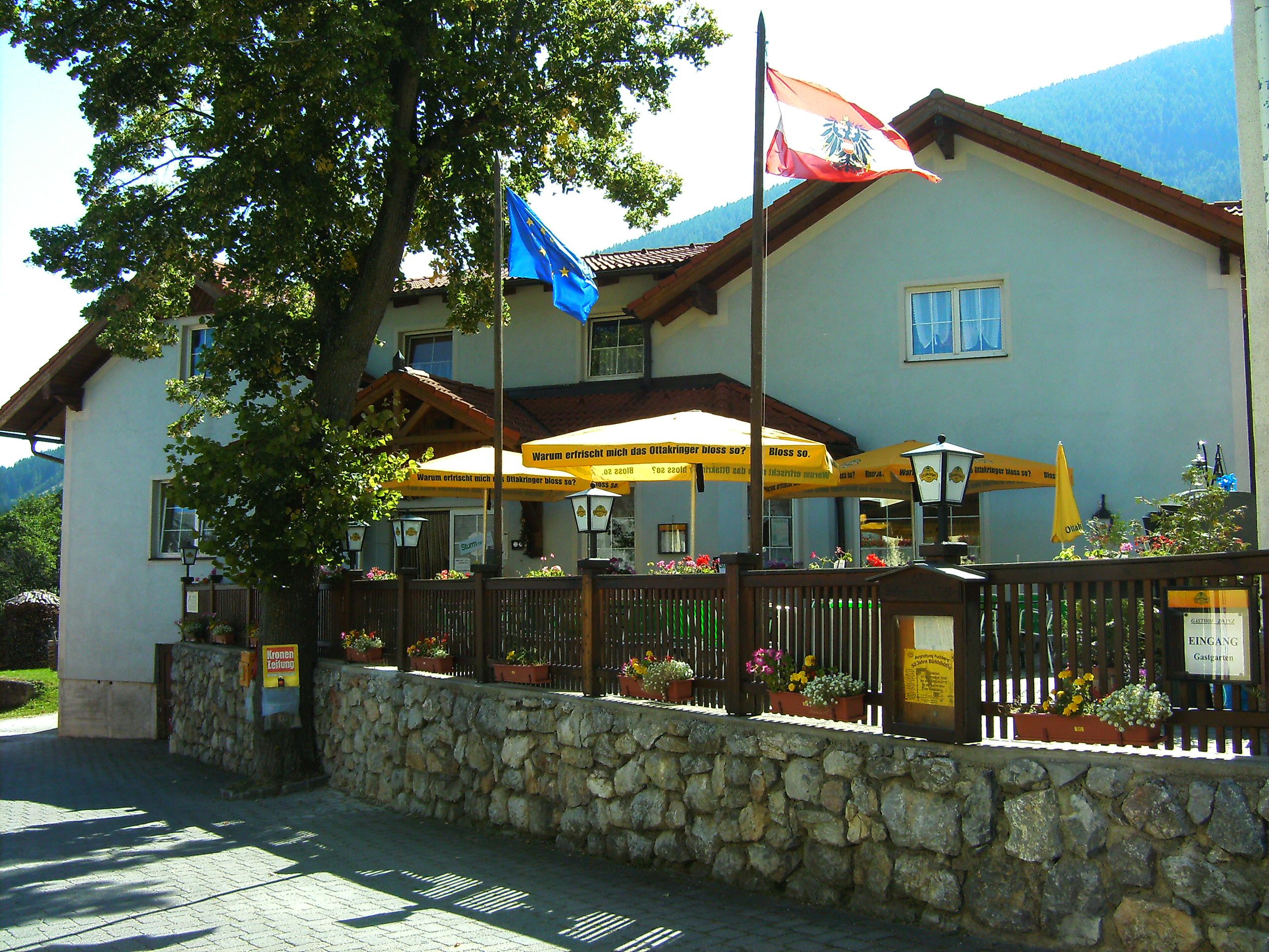 Gasthof Zwinz mit Terrasse und Sonnenschirmen, umgeben von Blumen und Fahnen.