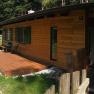Ein Holzferienhaus mit Terrasse in einer gr&uuml;nen, bewaldeten Umgebung.