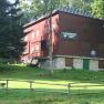 Piros sz&iacute;nű, faburkolatos &eacute;p&uuml;let, f&aacute;kkal &eacute;s r&eacute;ttel k&ouml;r&uuml;lv&eacute;ve, "Naturfreundehaus Ortsgruppe Ternitz" felirattal.