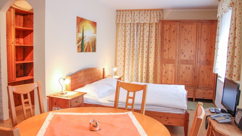 Small apartment with wooden furniture, bed, table and wardrobe.