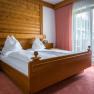 Ein gem&uuml;tliches Schlafzimmer mit einem Doppelbett aus Holz, wei&szlig;en Bettdecken und roten Vorh&auml;ngen vor einem Fenster.