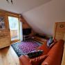 Gem&uuml;tliches Wohnzimmer mit rotem Ledersofa, buntem Teppich und Holzw&auml;nden in einem Ferienhaus.
