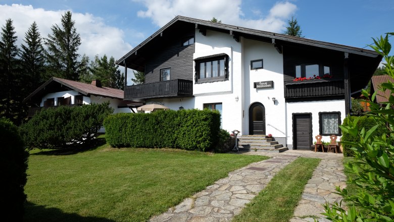 Ein zweist&ouml;ckiges Haus mit schwarzem Holz und wei&szlig;en W&auml;nden, umgeben von einem gepflegten Garten und B&auml;umen.