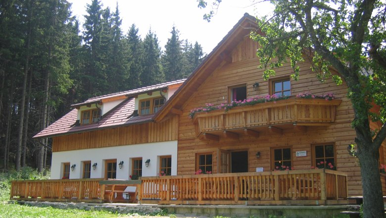 Eine rustikale Bergh&uuml;tte aus Holz mit Balkon und Terrasse, umgeben von B&auml;umen.