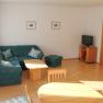 Wohnzimmer mit gr&uuml;ner Eckcouch, Holztisch, Fernseher und Esstisch.